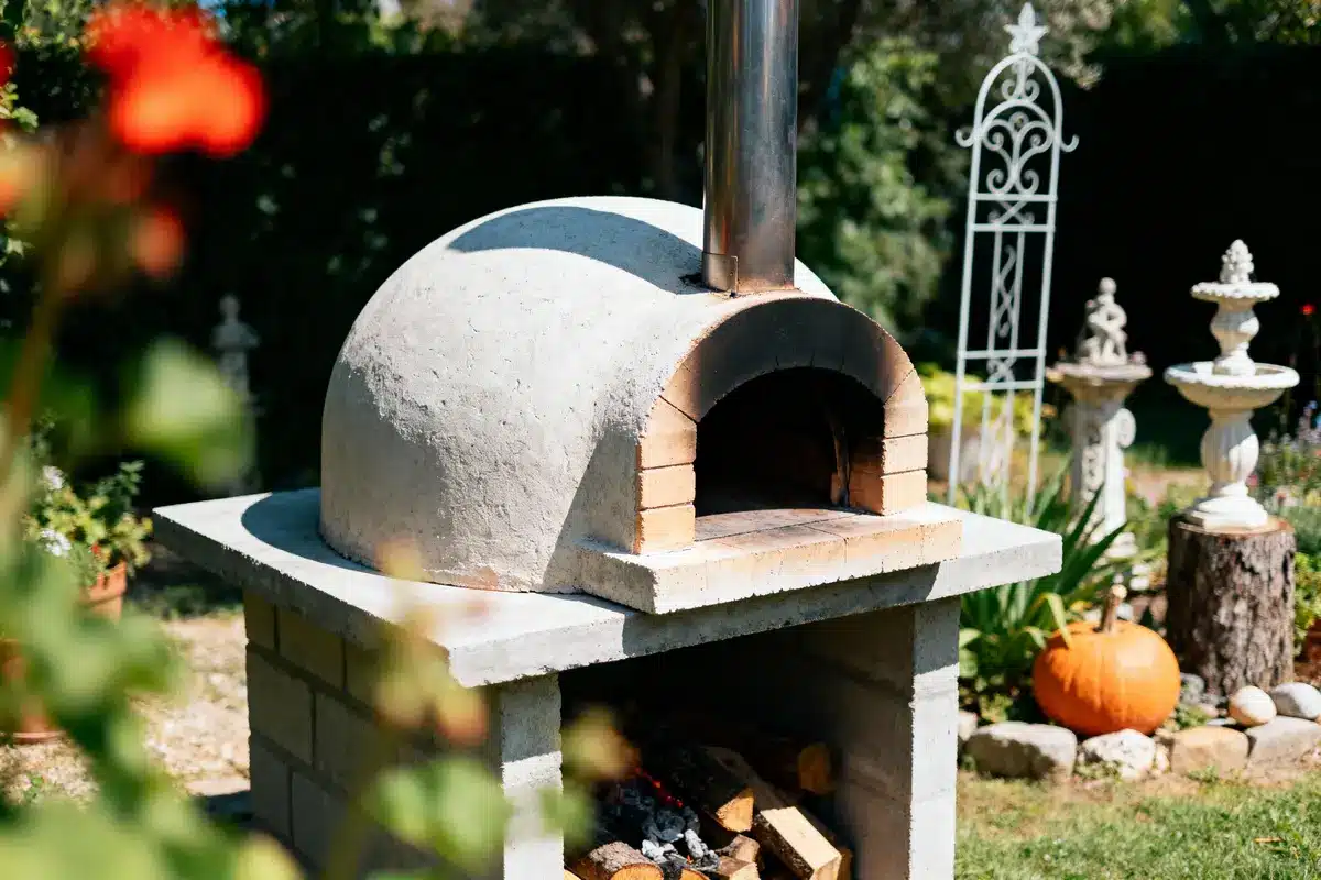 Four à pizza extérieur en pierre, jardin décoré avec citrouille, meubles de jardin en arrière-plan.
