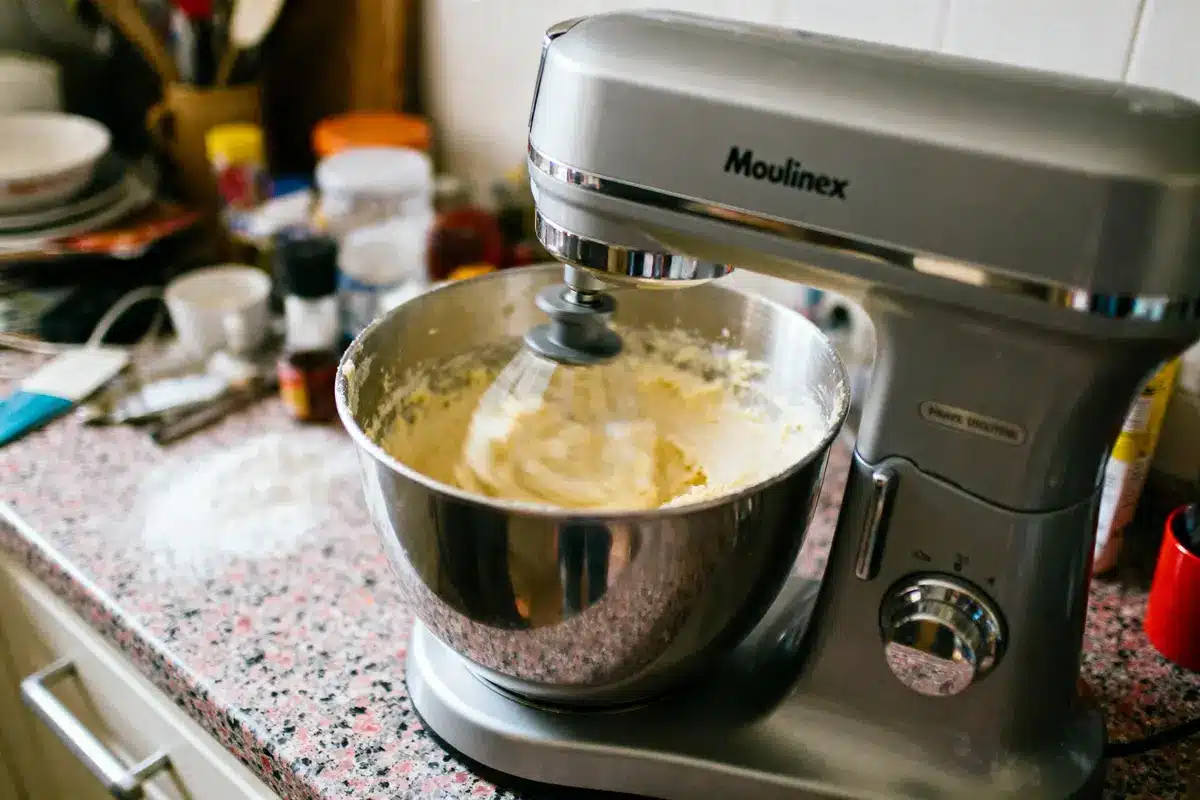 Mixeur de cuisine Moulinex sur plan de travail, mélangeant pâte dans bol, ingrédients en arrière-plan.