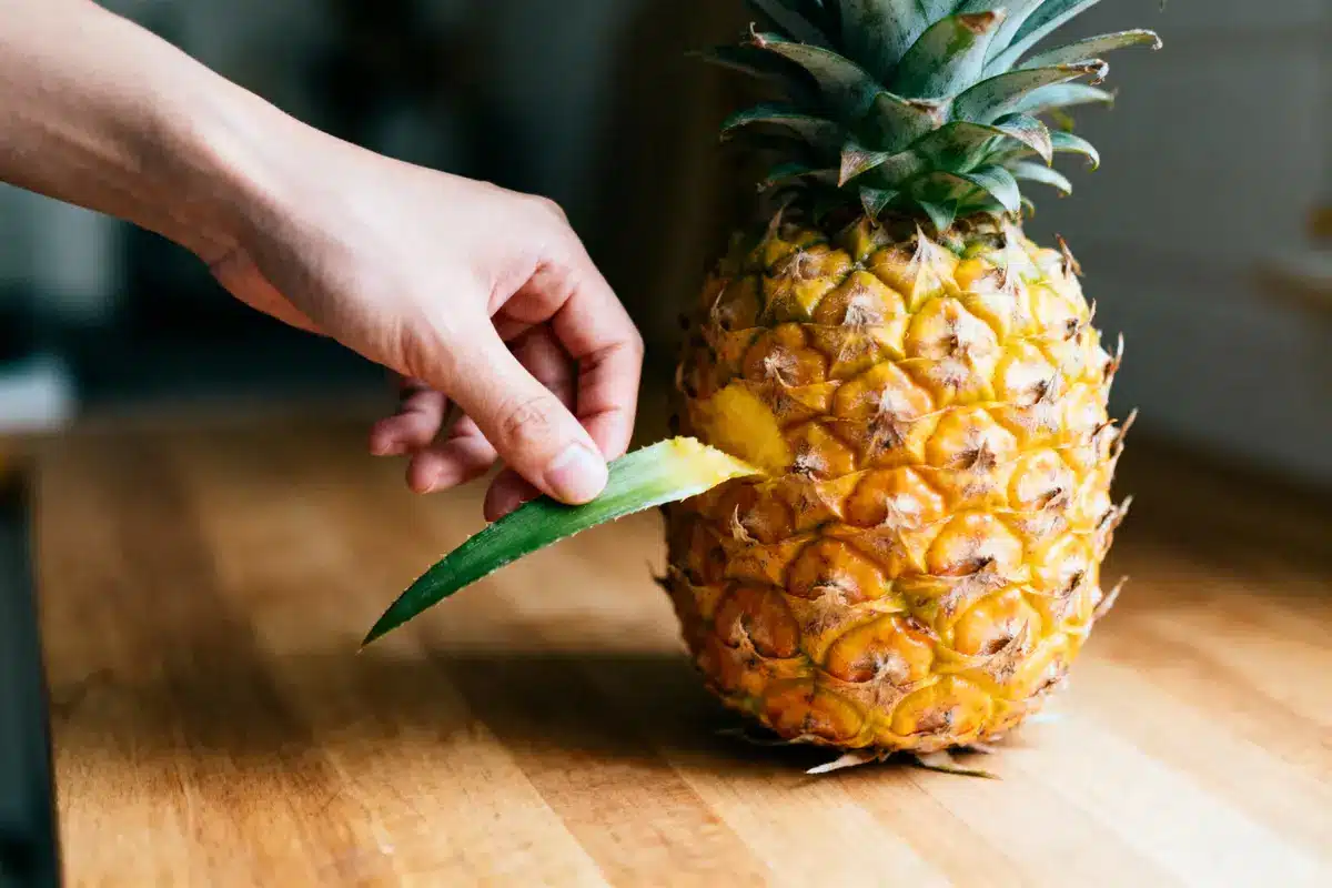 Main retirant une feuille d'ananas sur une table en bois.