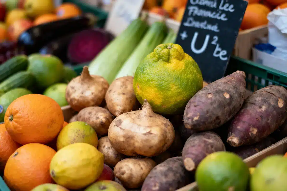 Fruits et légumes variés sur étal de marché, y compris oranges, citrons, patates douces, et cédrat.