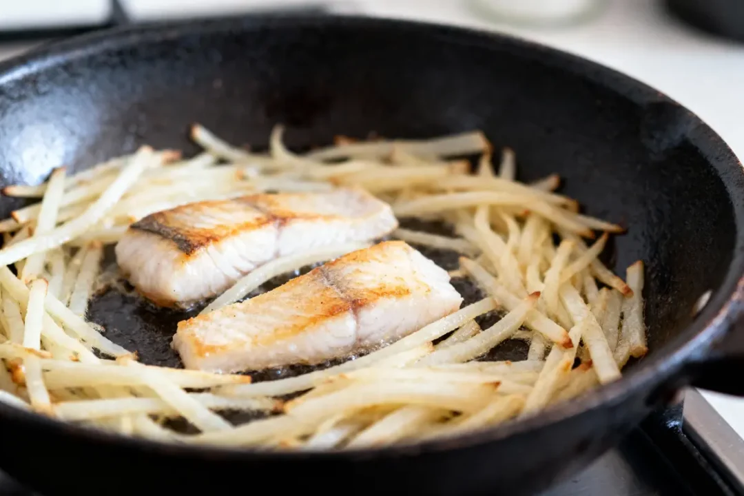 Poisson grillé avec des frites de pommes de terre dans une poêle en fonte noire.