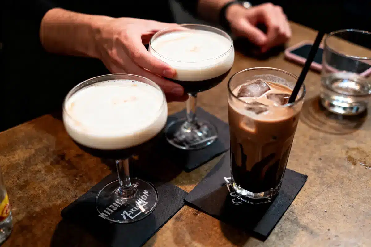 Trois cocktails sur table en bois, deux en coupes, un en verre avec glaçons et paille.