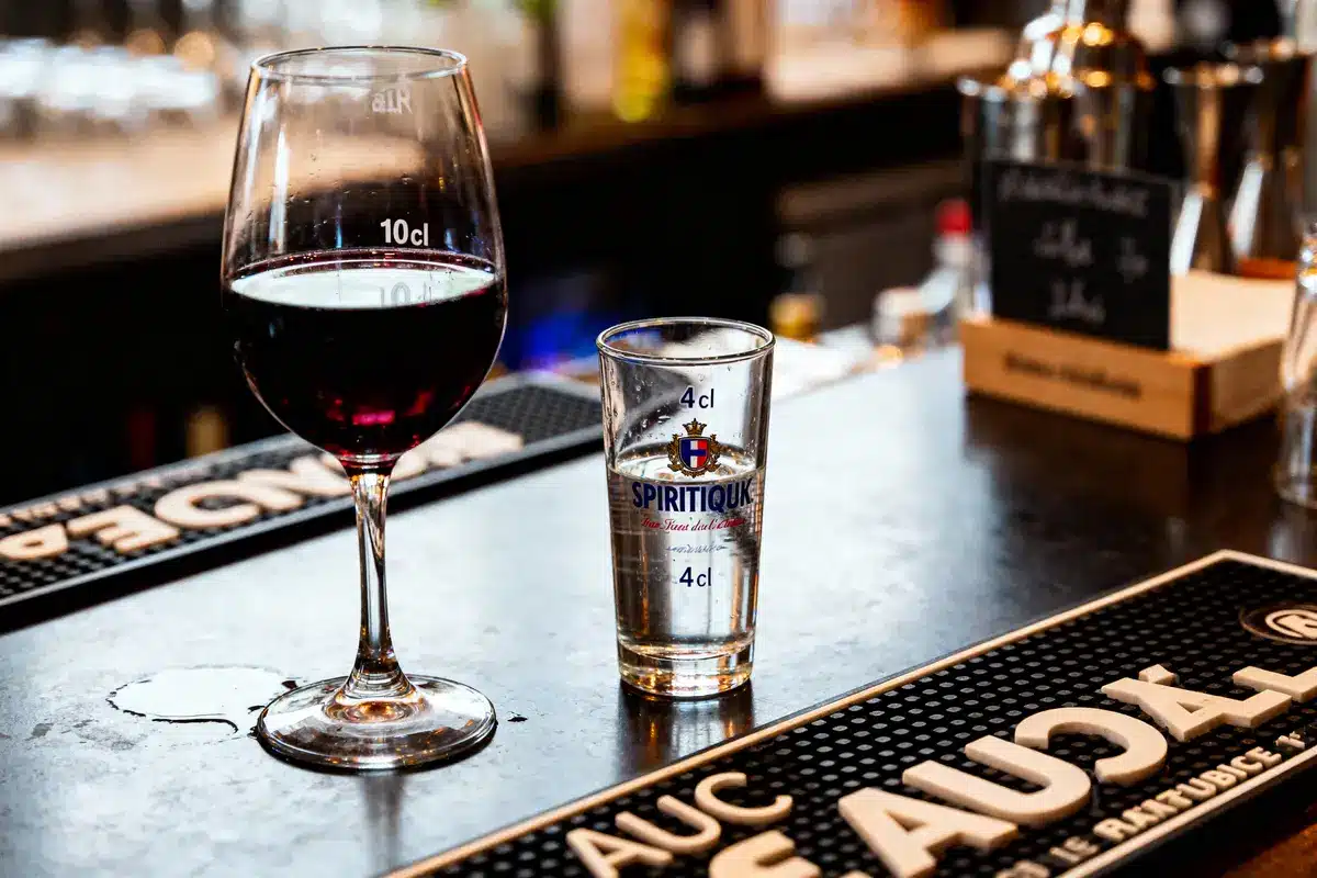 Verre de vin rouge et verre à spiritueux sur un comptoir de bar sombre.