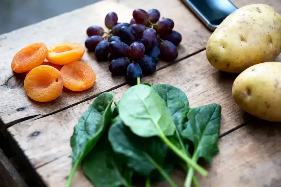 Abricots, raisins, épinards et pommes de terre sur une table en bois, smartphone en arrière-plan.