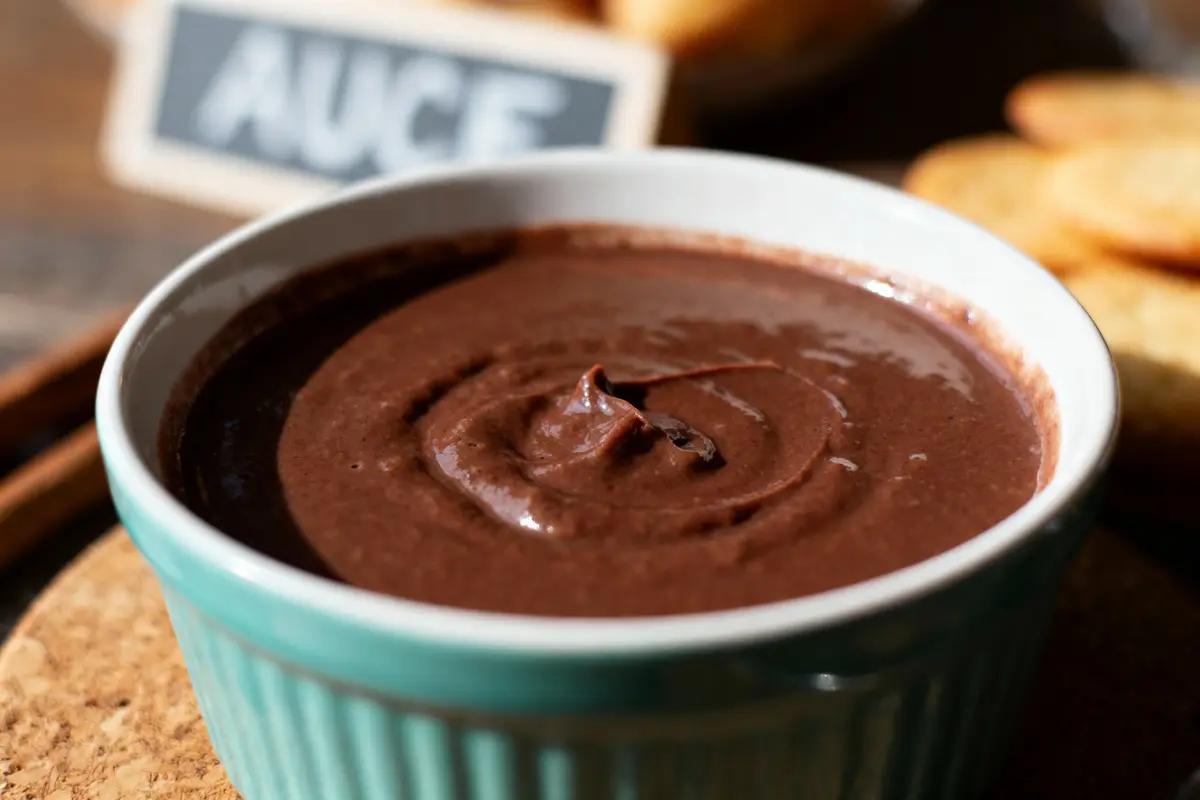 Bol en céramique bleue contenant une sauce chocolat onctueuse, étiquette floue en arrière-plan.