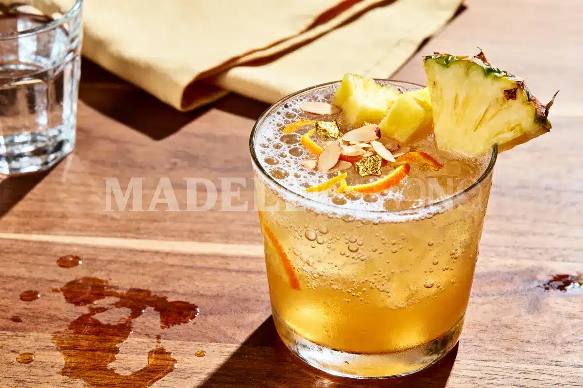 Verre de cocktail sur table en bois, ananas en garniture, serviette jaune en arrière-plan.