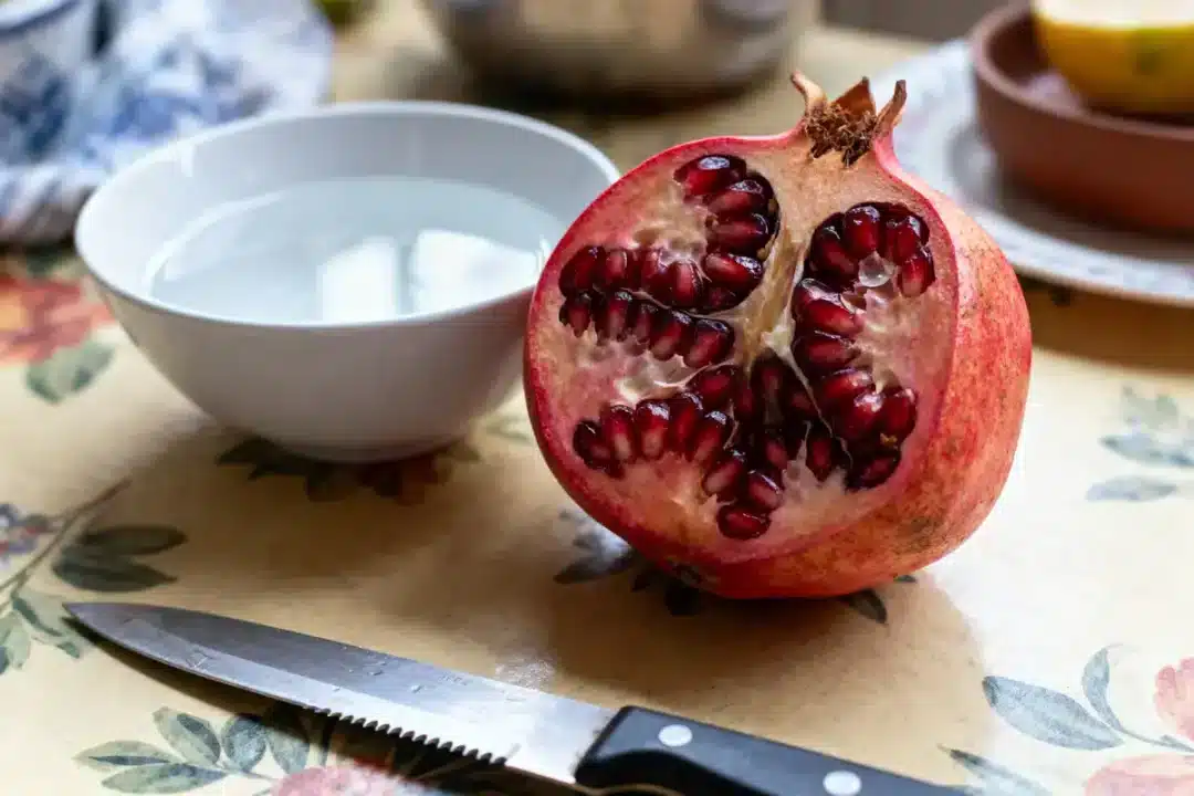 Demi-grenade ouverte, couteau et bol d'eau sur table à motif floral.