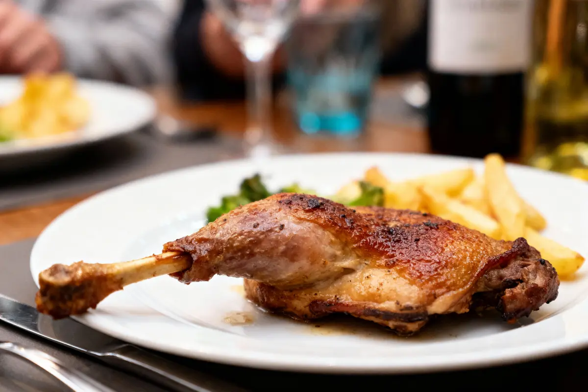 Assiette avec cuisse de poulet rôti, frites et légumes. Repas convivial sur une table.