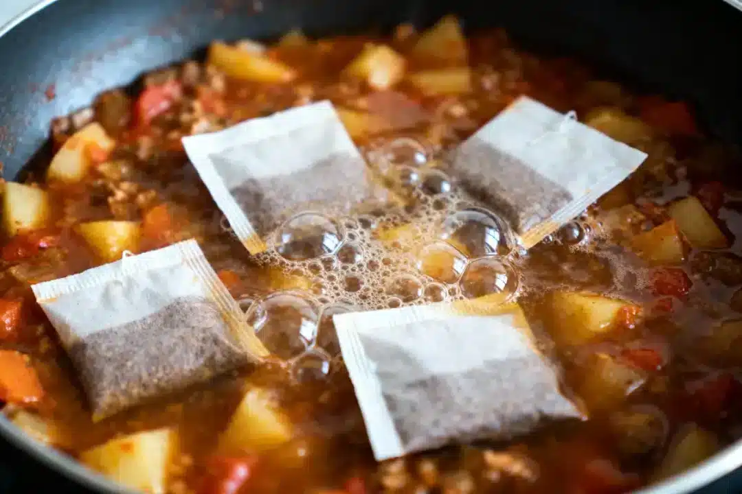 Ragoût avec pommes de terre, tomates et quatre sachets de thé sur le dessus, dans une poêle.