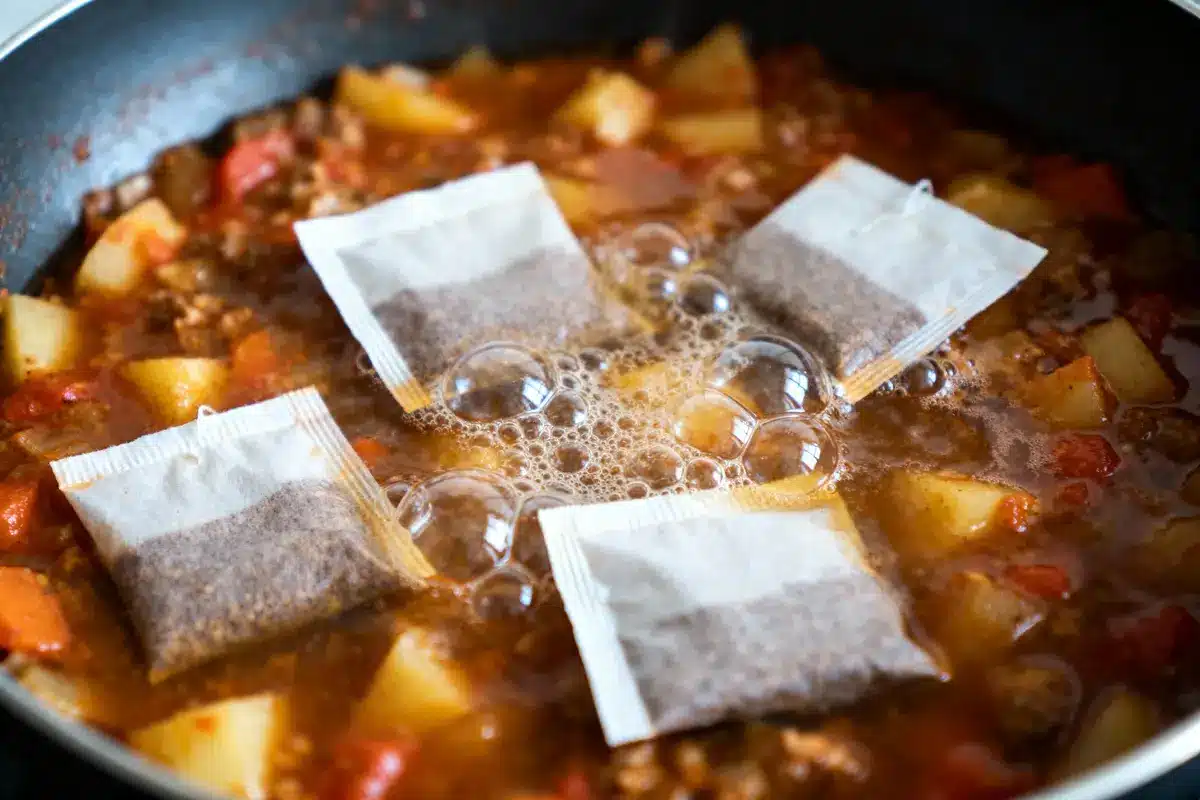 Ragoût avec pommes de terre, tomates et quatre sachets de thé sur le dessus, dans une poêle.
