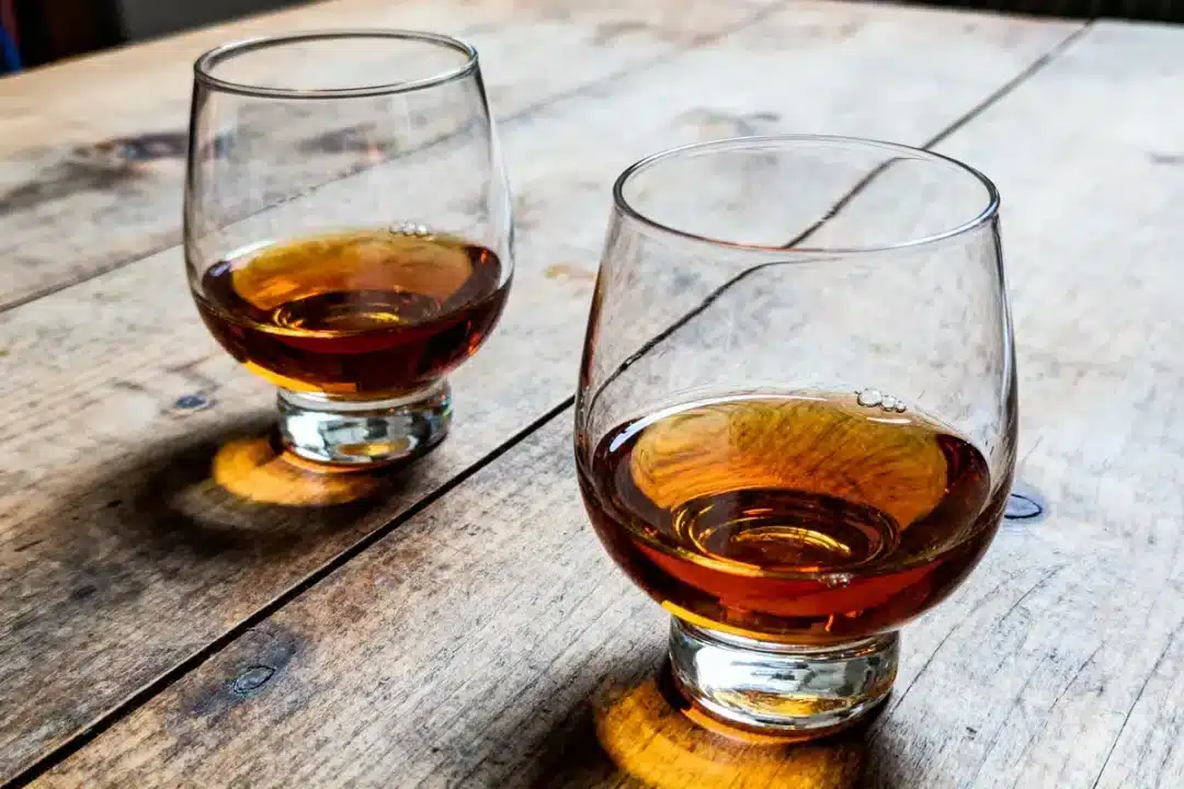 Deux verres de whisky ambré sur une table en bois rustique.