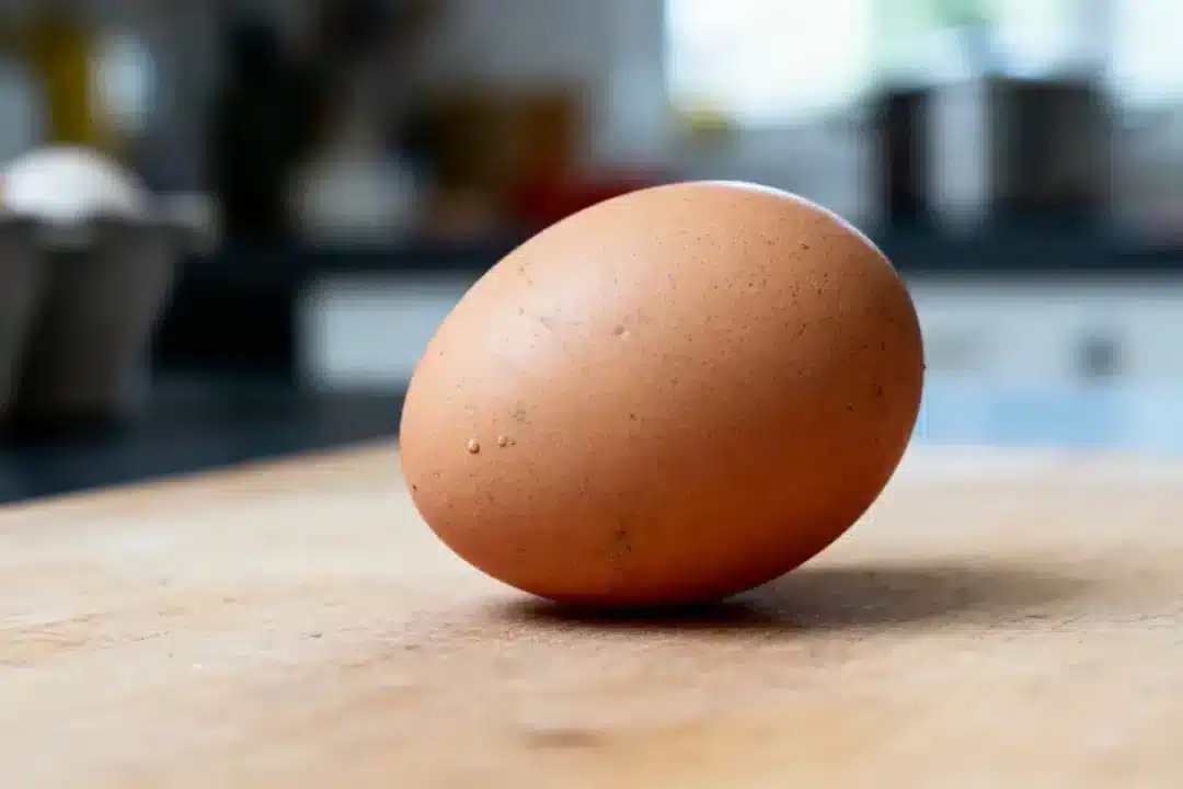 Un œuf brun posé sur une planche en bois dans une cuisine.