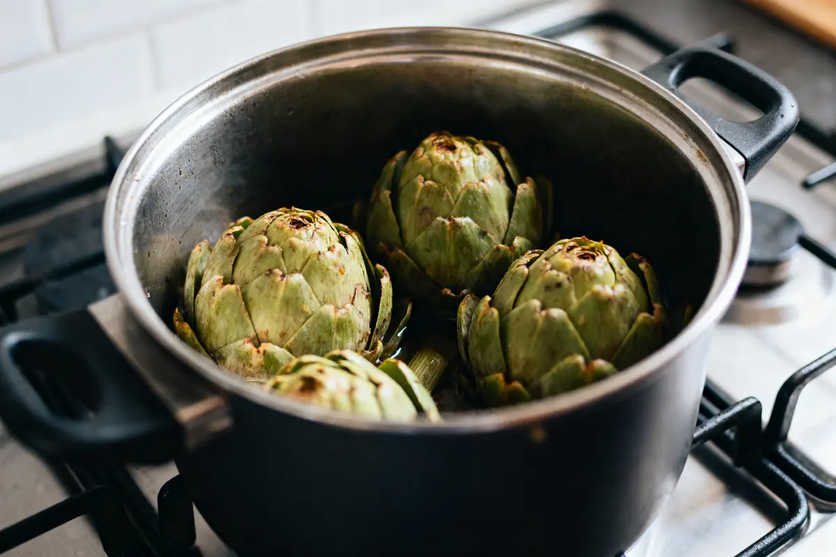 Quatre artichauts cuisant dans une grande casserole sur une cuisinière.