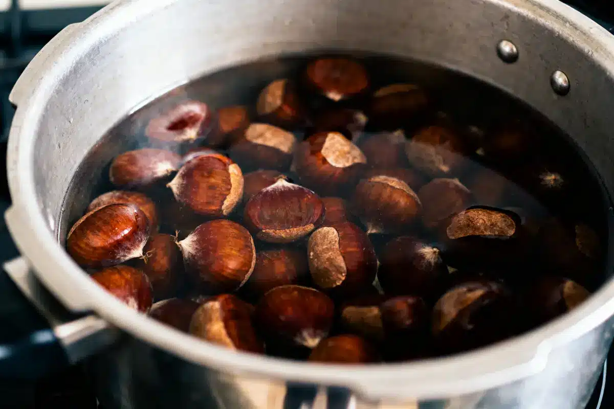 Châtaignes en train de bouillir dans une casserole en métal sur une cuisinière, avec de la vapeur visible.