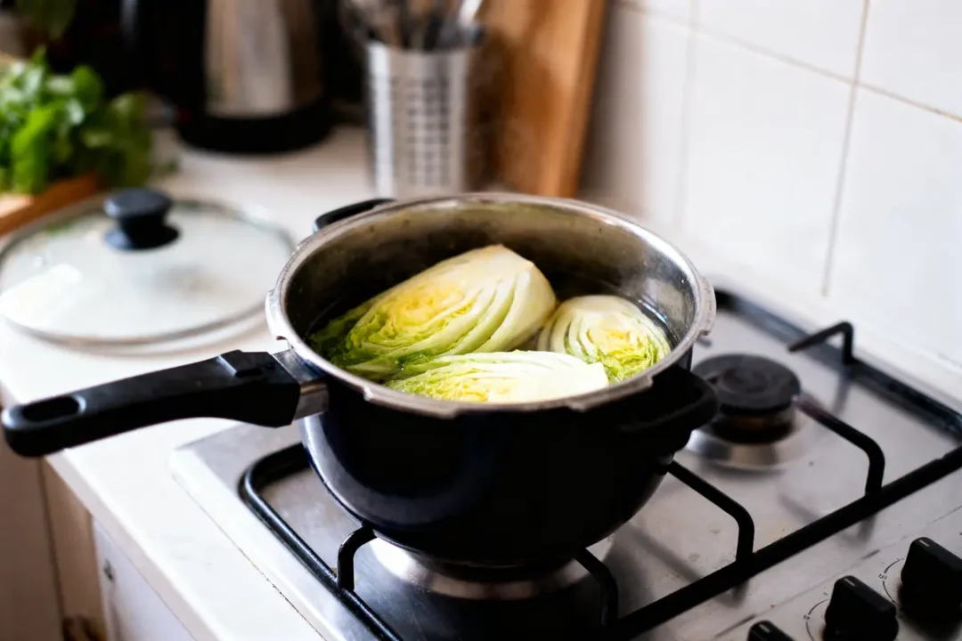 Choux coupés en deux cuisinant dans une cocotte sur une cuisinière, cuisine domestique en arrière-plan.