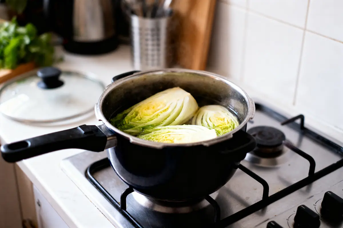 Choux coupés en deux cuisinant dans une cocotte sur une cuisinière, cuisine domestique en arrière-plan.