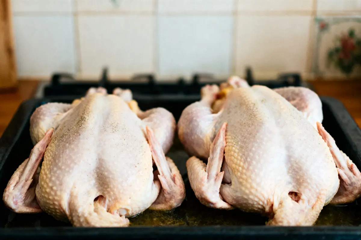 Deux canards crus sur une plaque de cuisson, prêts à être préparés. Cuisine en arrière-plan.