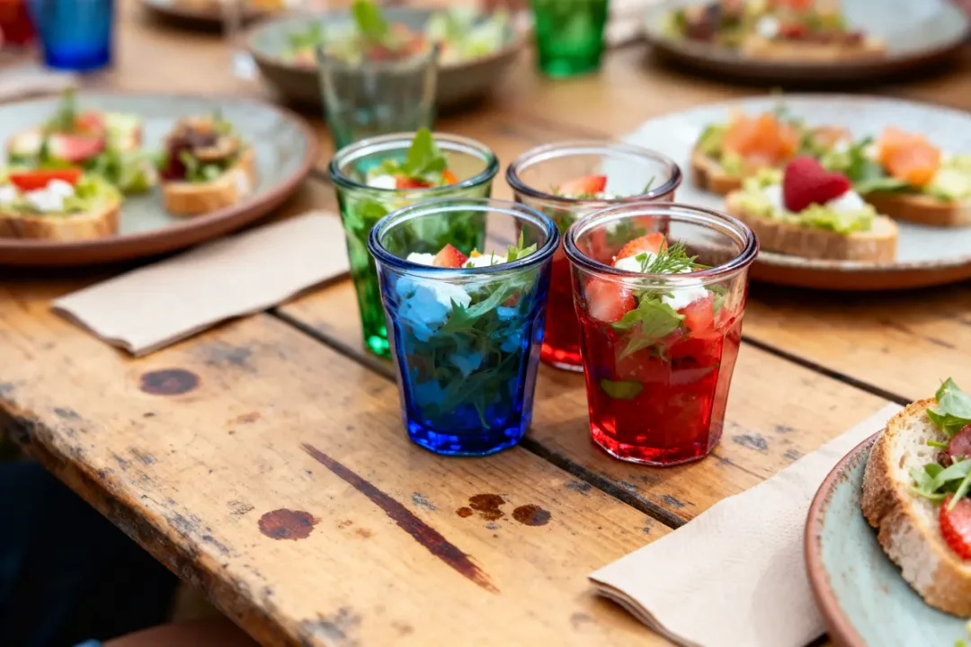 Verres colorés avec salade et assiettes de bruschetta sur une table en bois.