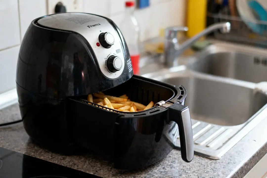 Friteuse à air noir sur un comptoir de cuisine avec des frites à l'intérieur.