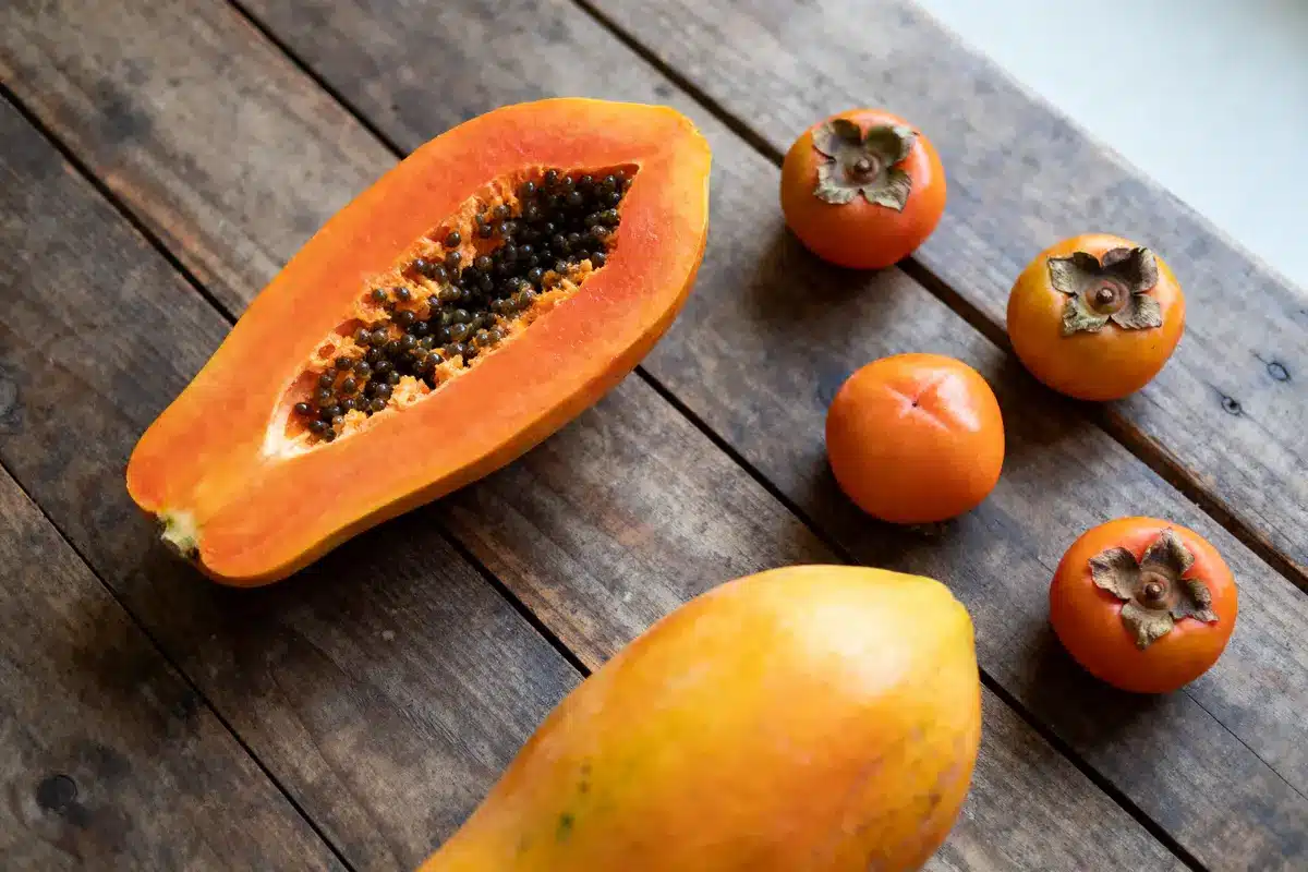 Papaye tranchée et kakis entiers sur une table en bois brun, éclairage naturel.