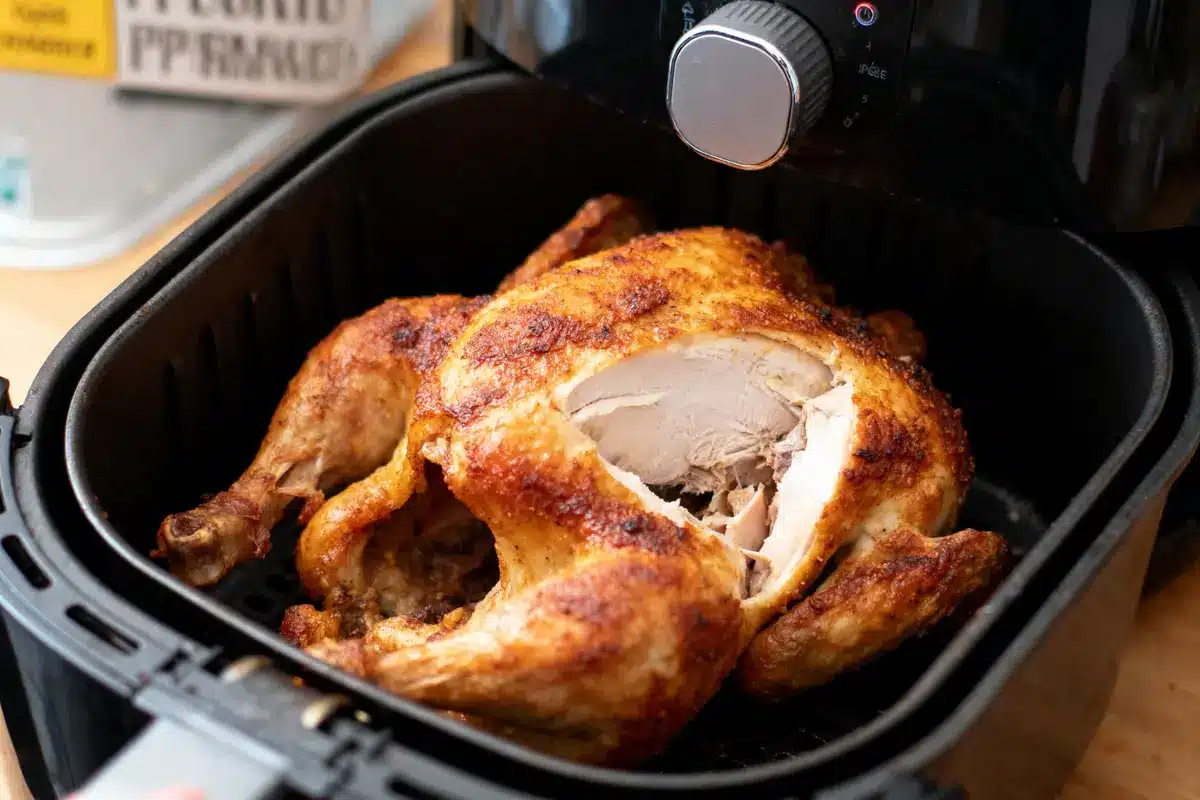 Poulet rôti doré dans une friteuse à air, partiellement découpé, montrant un intérieur juteux et savoureux.