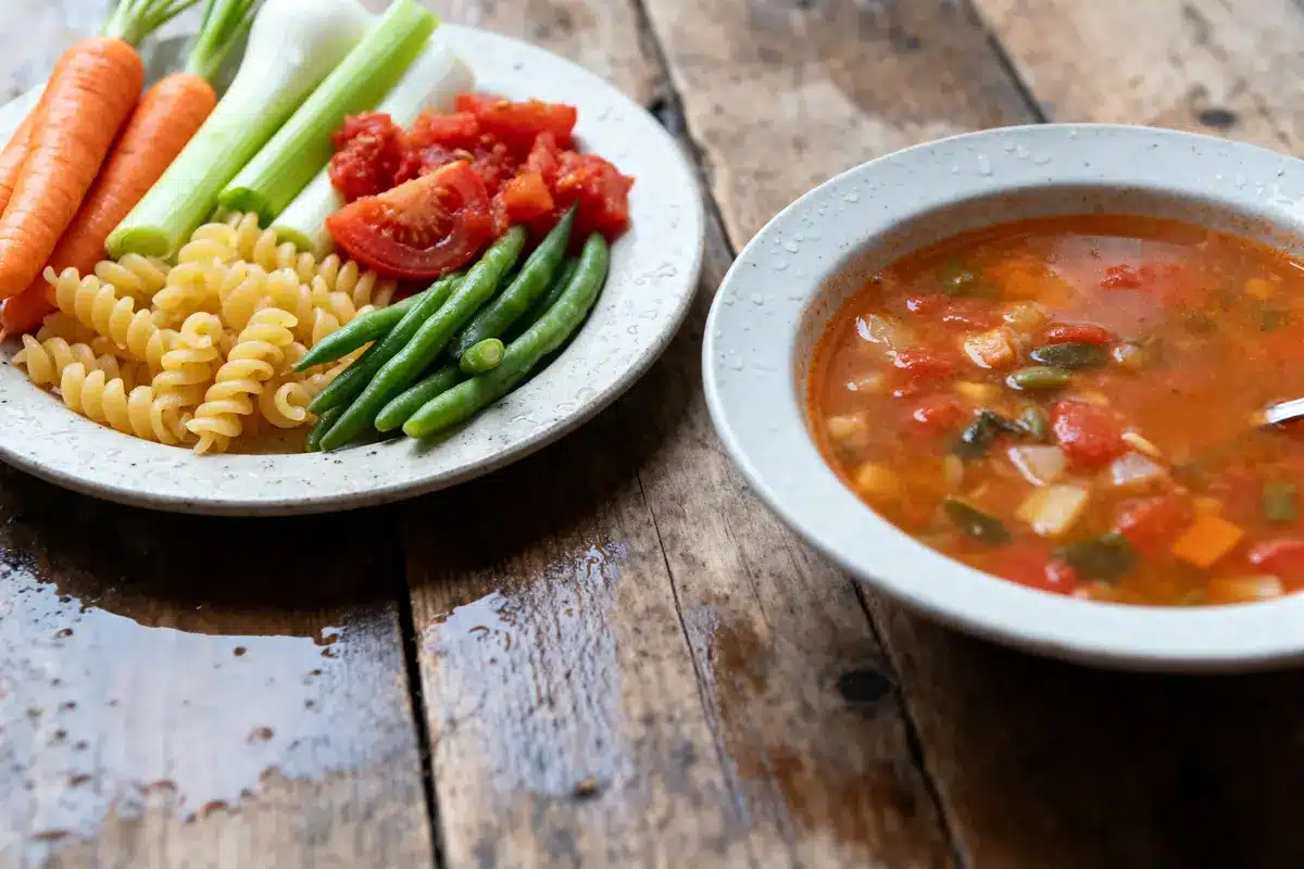 Assiette de légumes et pâtes crues, soupe aux légumes dans un bol, sur table en bois.
