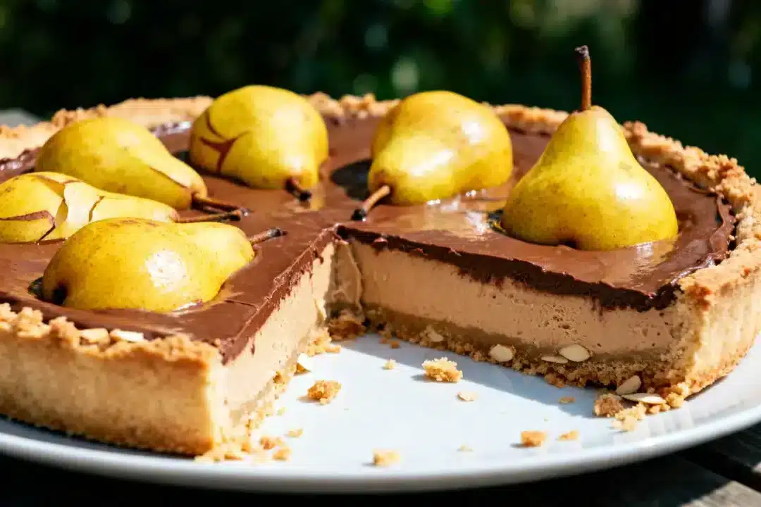 Tarte chocolat aux poires entières, part coupée, croûte biscuitée, sur assiette blanche, fond flou.