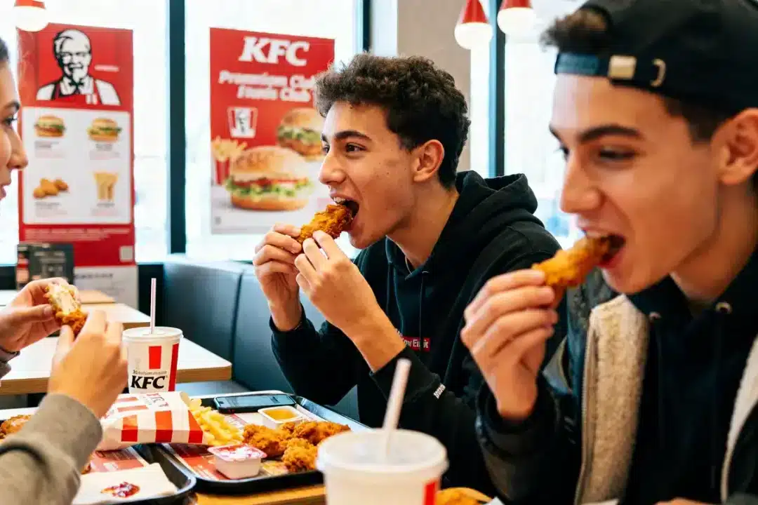 Des jeunes savourant du poulet KFC gratuit dans un restaurant avec boissons et frites.