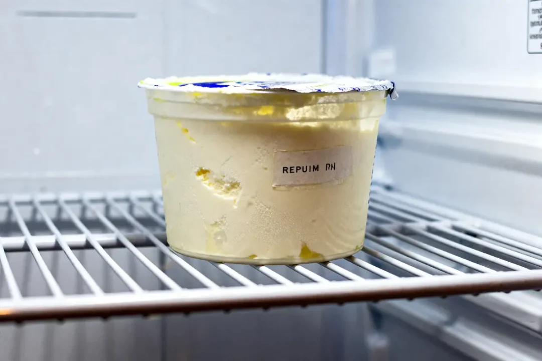 Pot de crème fraîche périmée dans un réfrigérateur avec couvercle abîmé et étiquette illisible