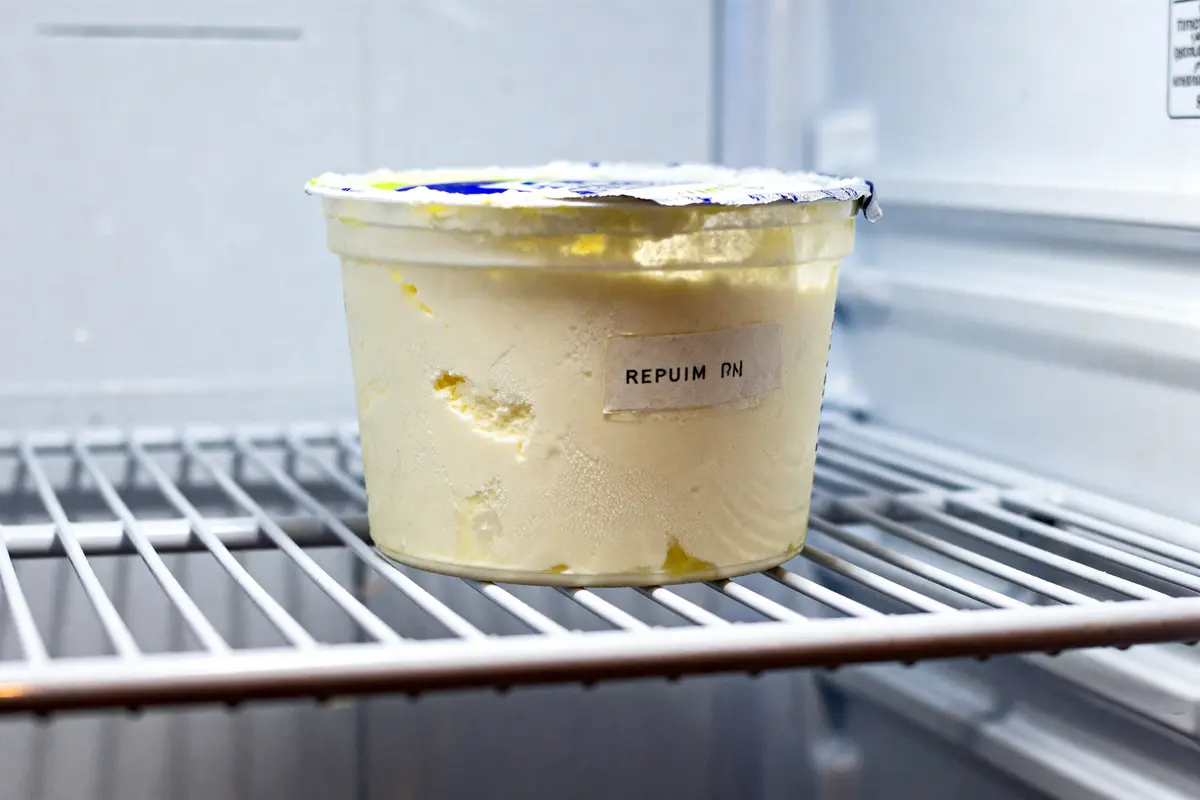 Pot de crème fraîche périmée dans un réfrigérateur avec couvercle abîmé et étiquette illisible