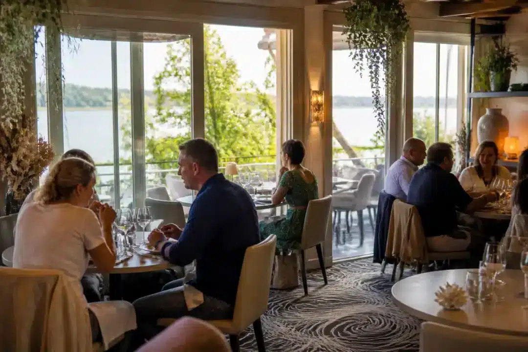 Salle de restaurant Villa Belle Rive avec vue sur le fleuve et convives dînant.